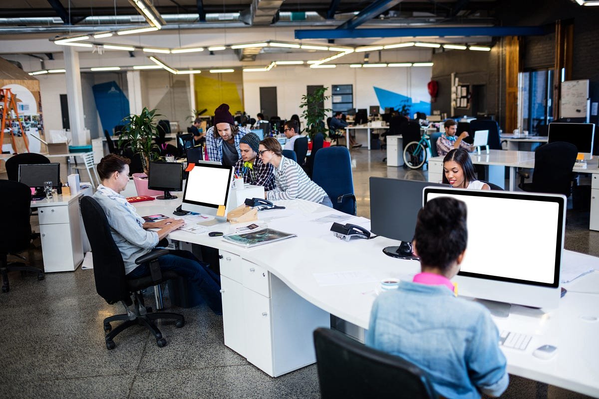 Open-plan coworking office with several people working at white curved desks and computers in bright, modern space