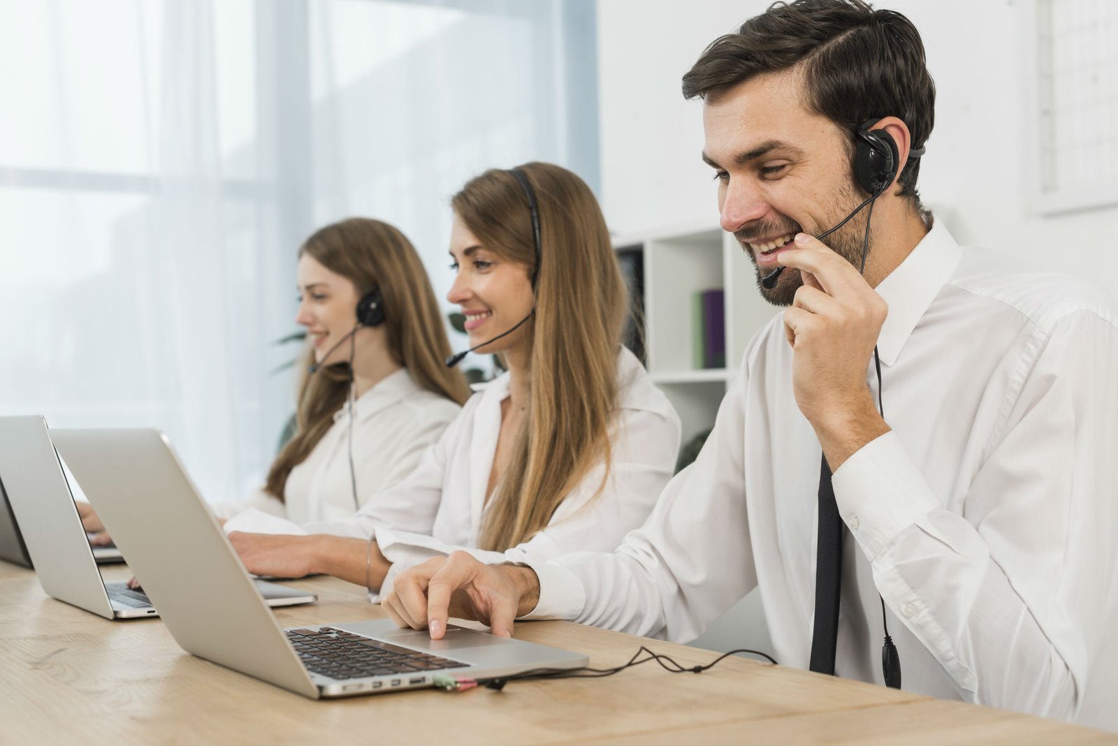 Three customer service agents wearing headsets and typing on laptops in an office.