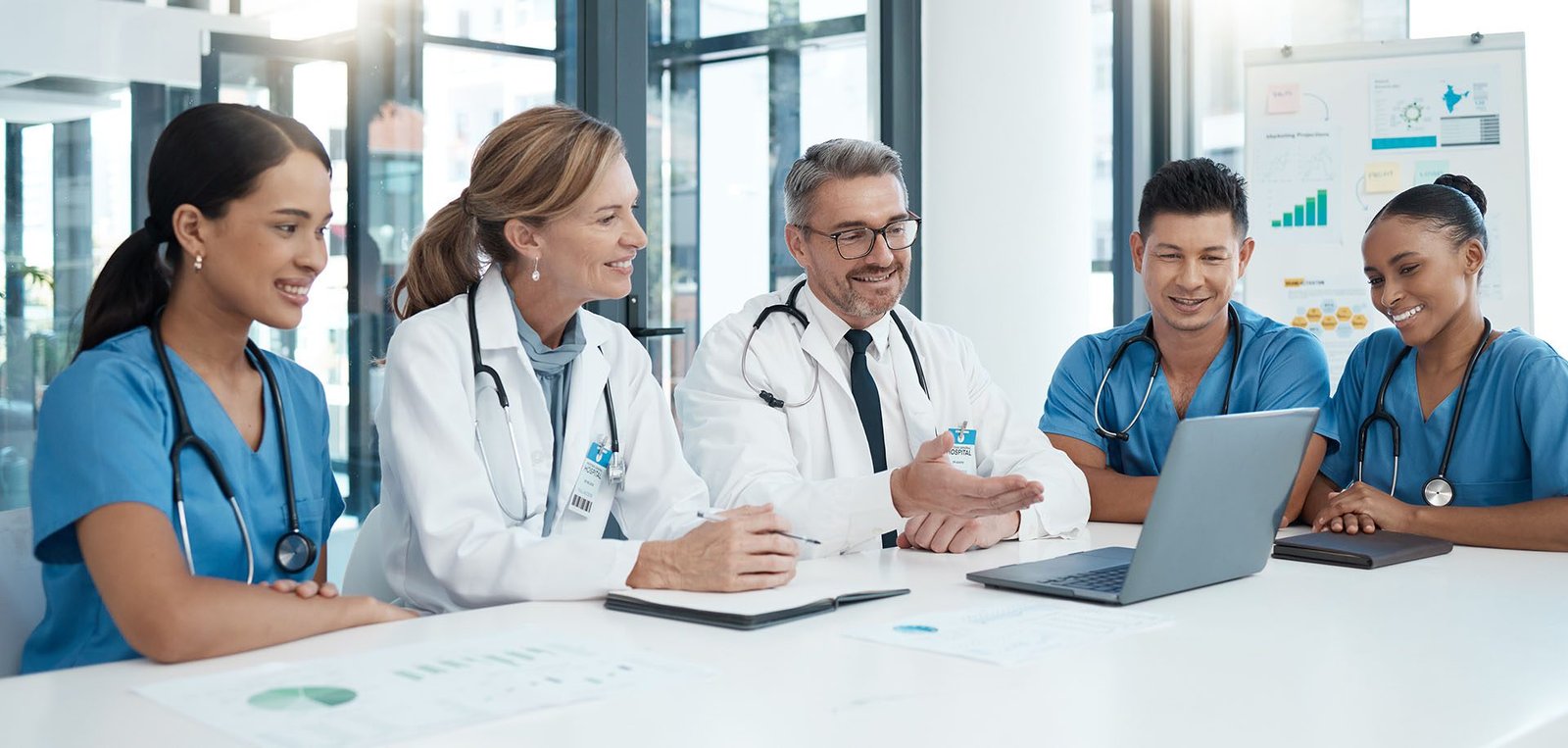 Medical team of doctors and nurses in a meeting around a table with a laptop and charts, collaborating