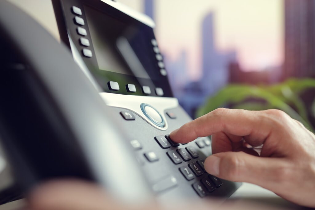Close-up of a finger pressing keypad buttons on a desk phone during a call.