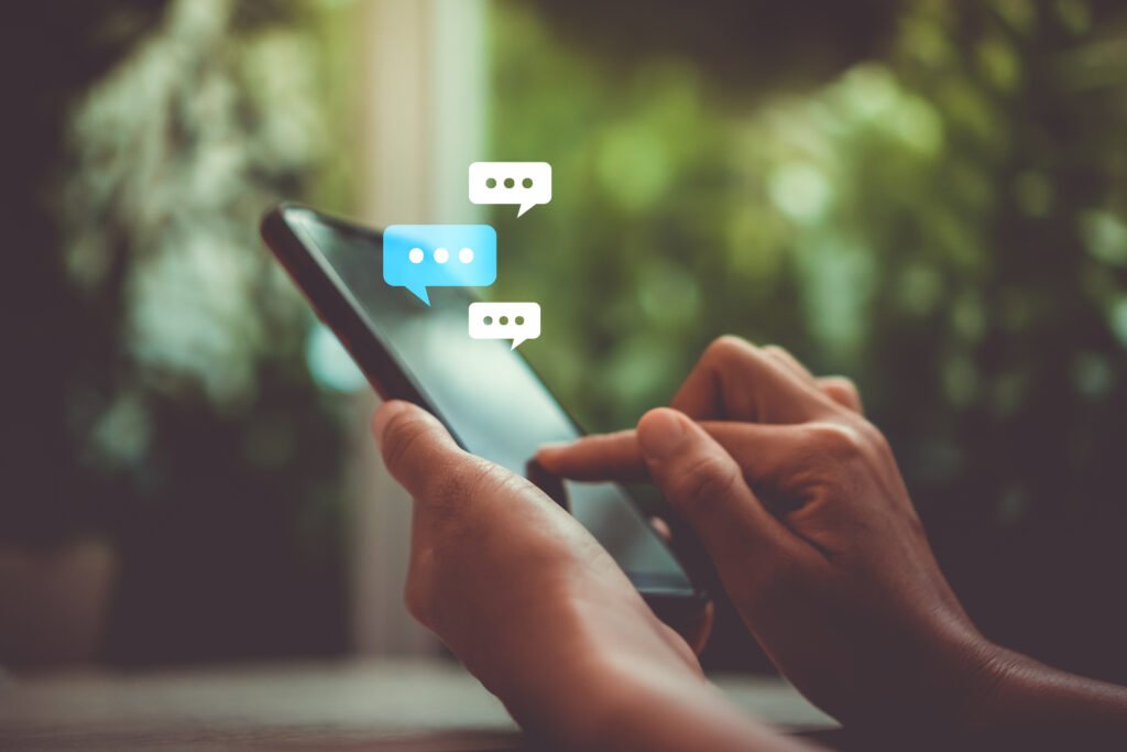 Close-up of hands holding a smartphone with floating chat bubbles over a blurred outdoor background.