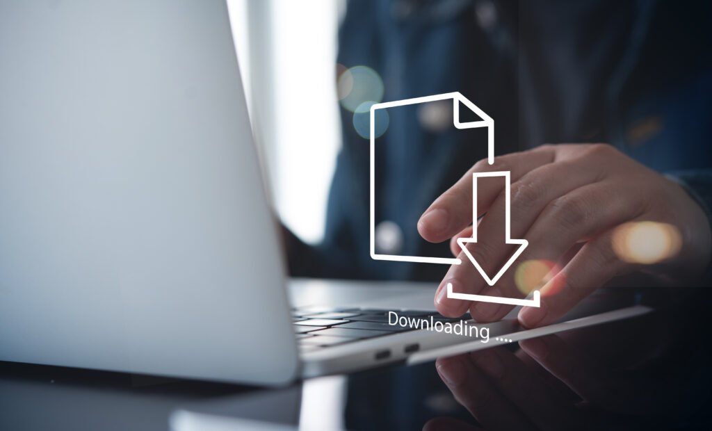 Person typing on a laptop with a large white download icon overlay and the word 'Downloading' text, indicating a file transfer in progress.