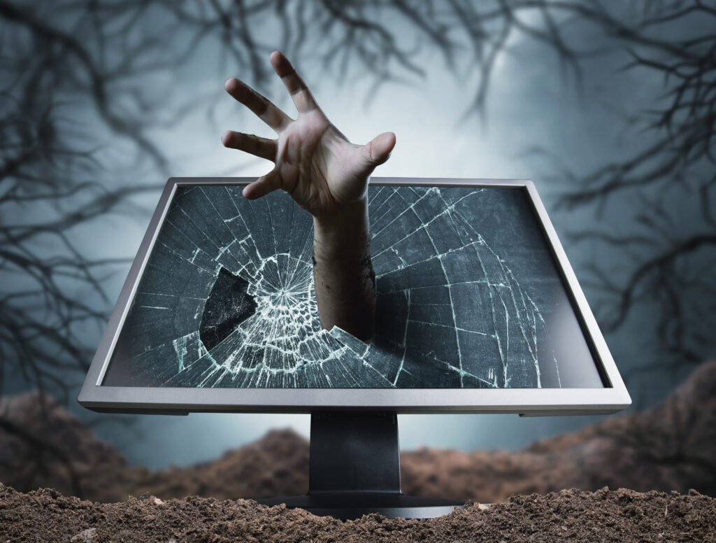 Hand reaching out from a cracked computer monitor, emerging from dirt in a dark, eerie setting.