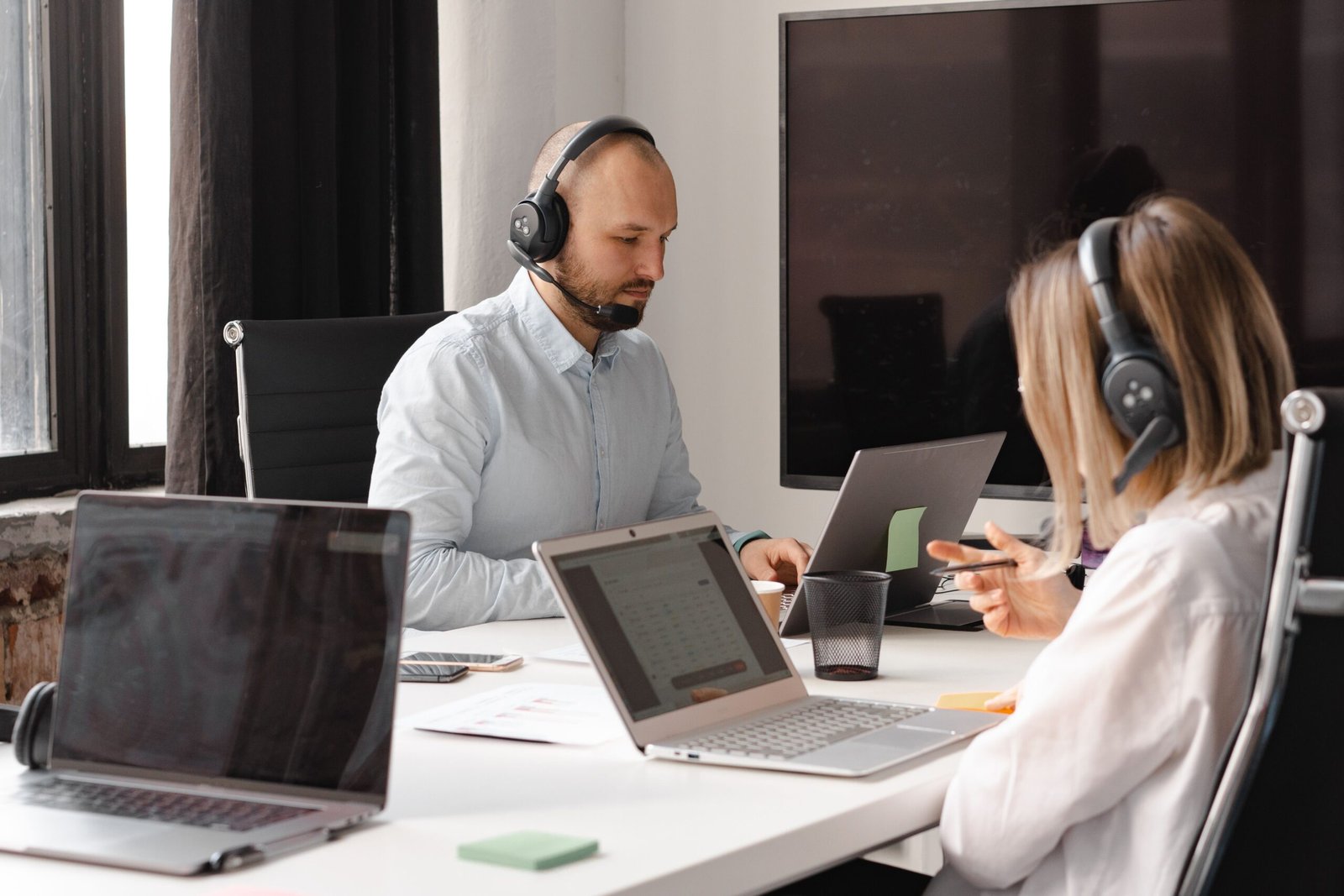 People in a meeting wearing headsets working on laptops around a conference table.